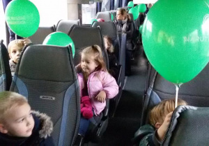 Widok na dzieci siedzące w autokarze z zielonymi balonami.